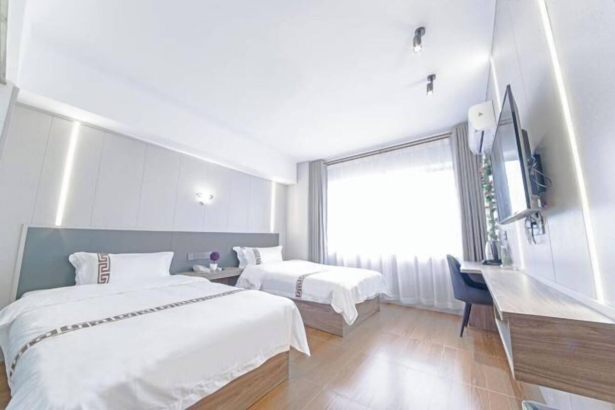 Une chambre d’hôtel avec deux lits, un bureau, un miroir et une grande fenêtre.