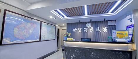 A reception desk with a digital screen, framed maps, and a clock.
