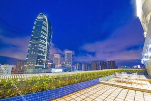 A rooftop terrace with a view of a city skyline, including a tall building and other high-rise structures.
