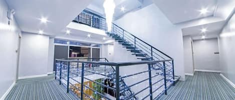 A spacious interior with a central staircase, a mezzanine level, and a view of the cityscape.