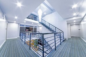 A spacious interior with a central staircase, a mezzanine level, and a view of the cityscape.
