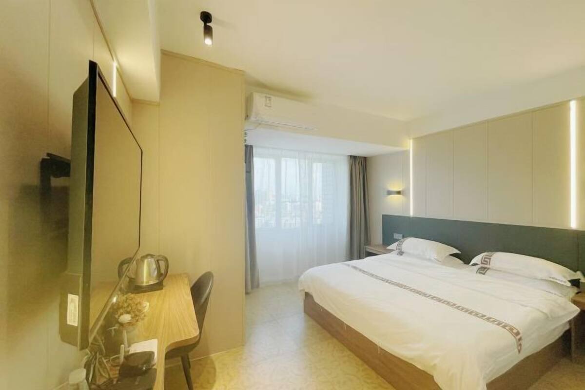 Une chambre d’hôtel comprenant un lit, un bureau avec une chaise, une télévision et une fenêtre avec des rideaux.