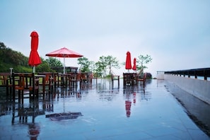 An outdoor seating area with tables and chairs, some with red umbrellas, on a wet surface. - Green Field Manor (Ningbo)