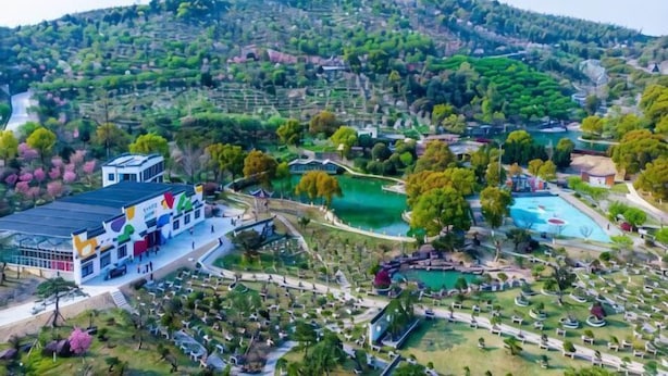 An aerial view of a resort with a swimming pool, landscaped gardens, and a building with a flat roof. - Green Field Manor (Ningbo)