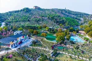 An aerial view of a resort with a swimming pool, landscaped gardens, and a building with a flat roof. - Green Field Manor (Ningbo)