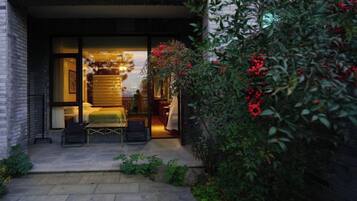 A modern building entrance with a glass door, a small outdoor seating area with a table and chairs, and a garden with red berries.