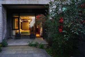 A modern building entrance with a glass door, a small outdoor seating area with a table and chairs, and a garden with red berries. - Green Field Manor (Ningbo)