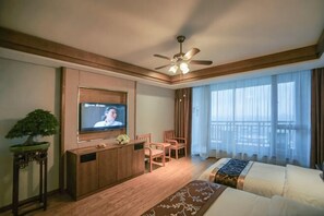 A hotel room with a TV, a sofa, a dining table, chairs, a ceiling fan, and a large window.
