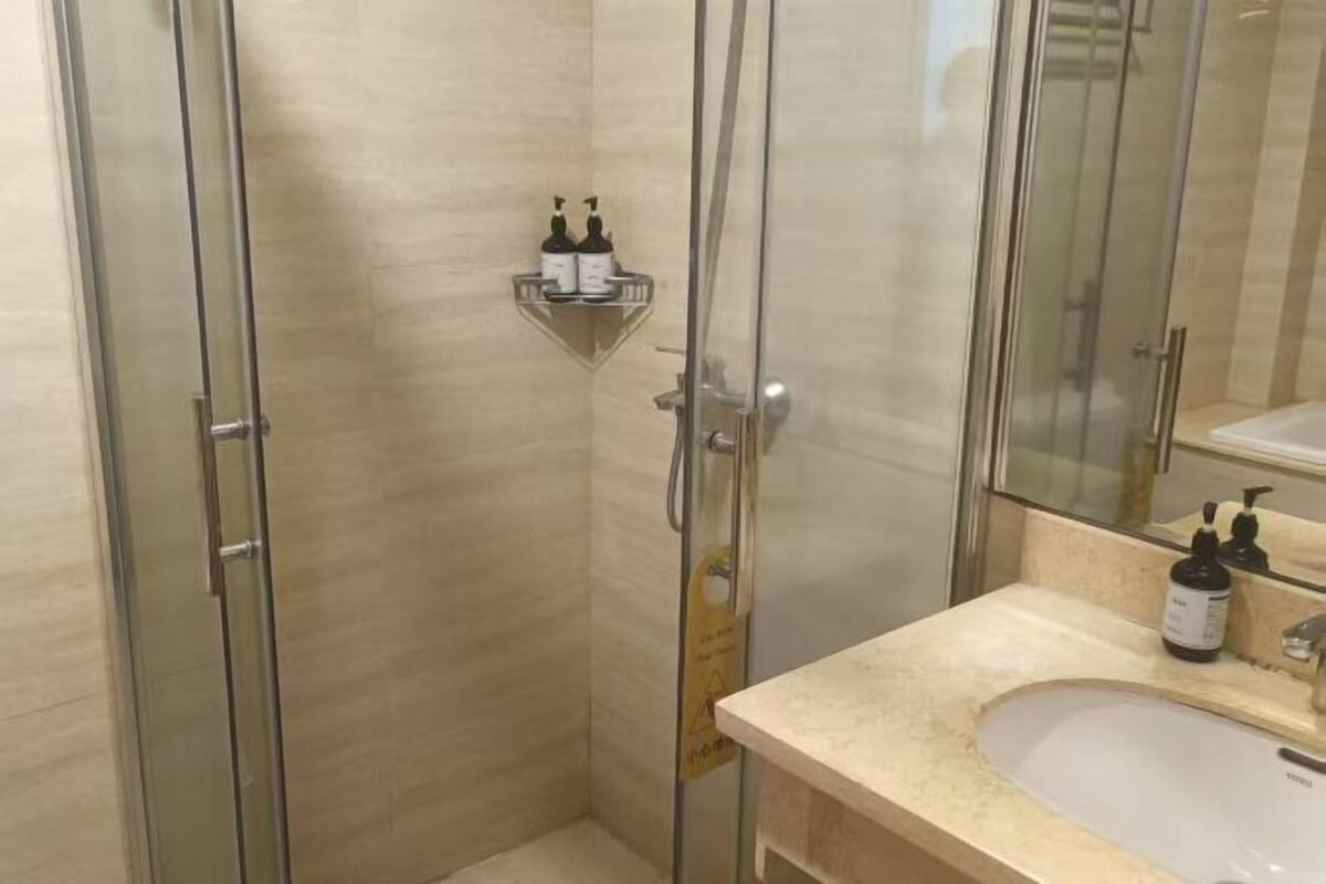 A modern bathroom with a glass shower enclosure, a beige countertop, and a mirror above the sink.