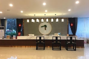 A hotel reception area with a marble counter, two black chairs, and a large circular wall decoration.