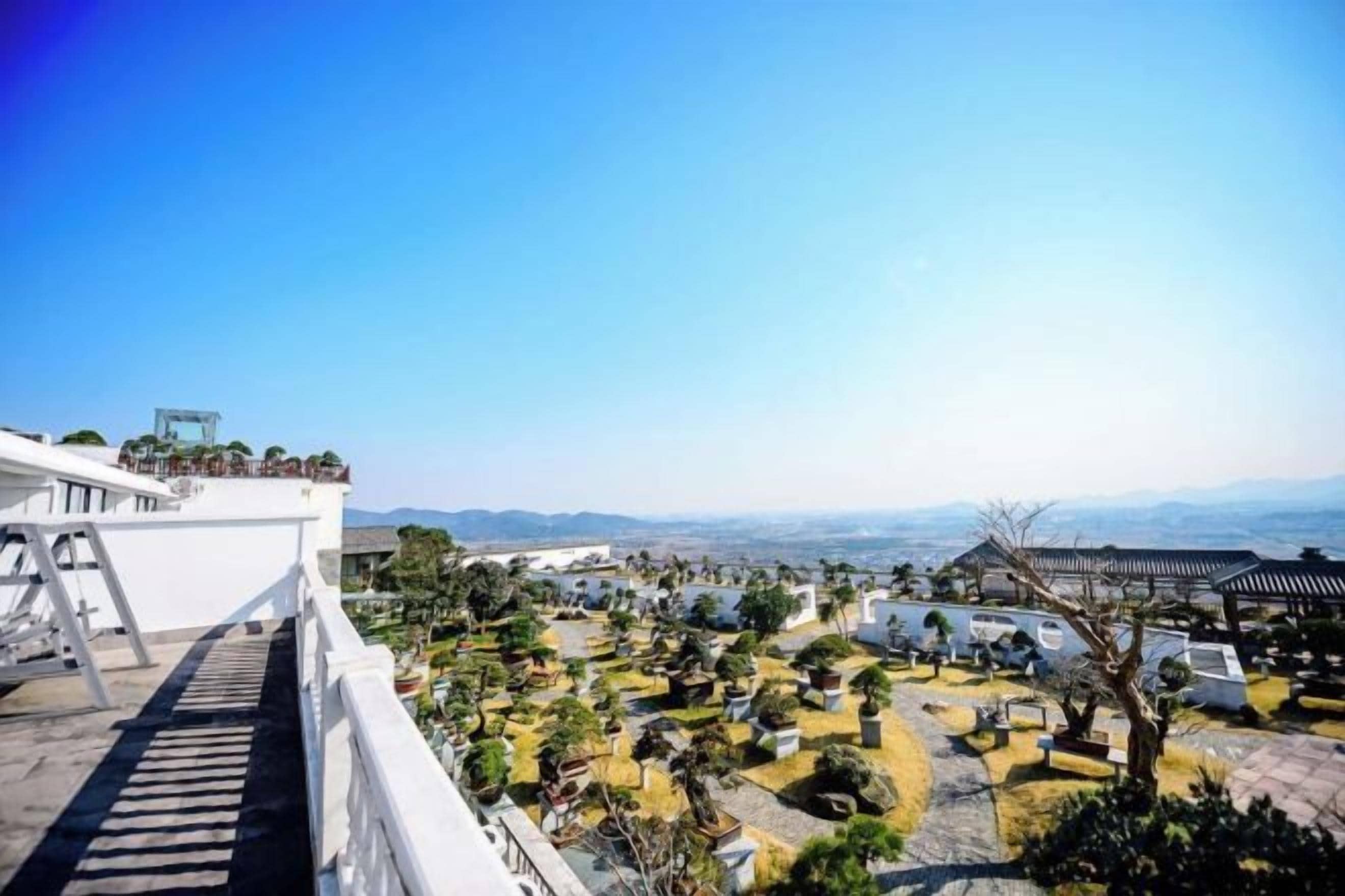 A panoramic view of a cemetery with a clear sky, featuring a white building with a balcony on the left and a traditional structure in the distance.
