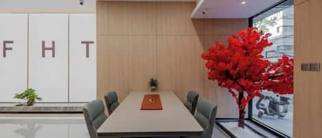 A modern conference room with a long table, four chairs, and a potted plant.