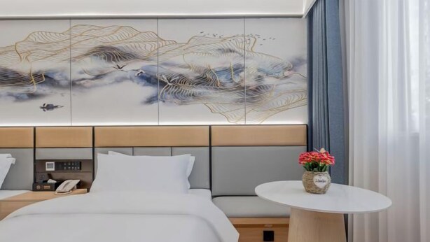 Habitación de hotel con cama, mesita de noche con teléfono, obra de arte en la pared y una pequeña mesa con flores.