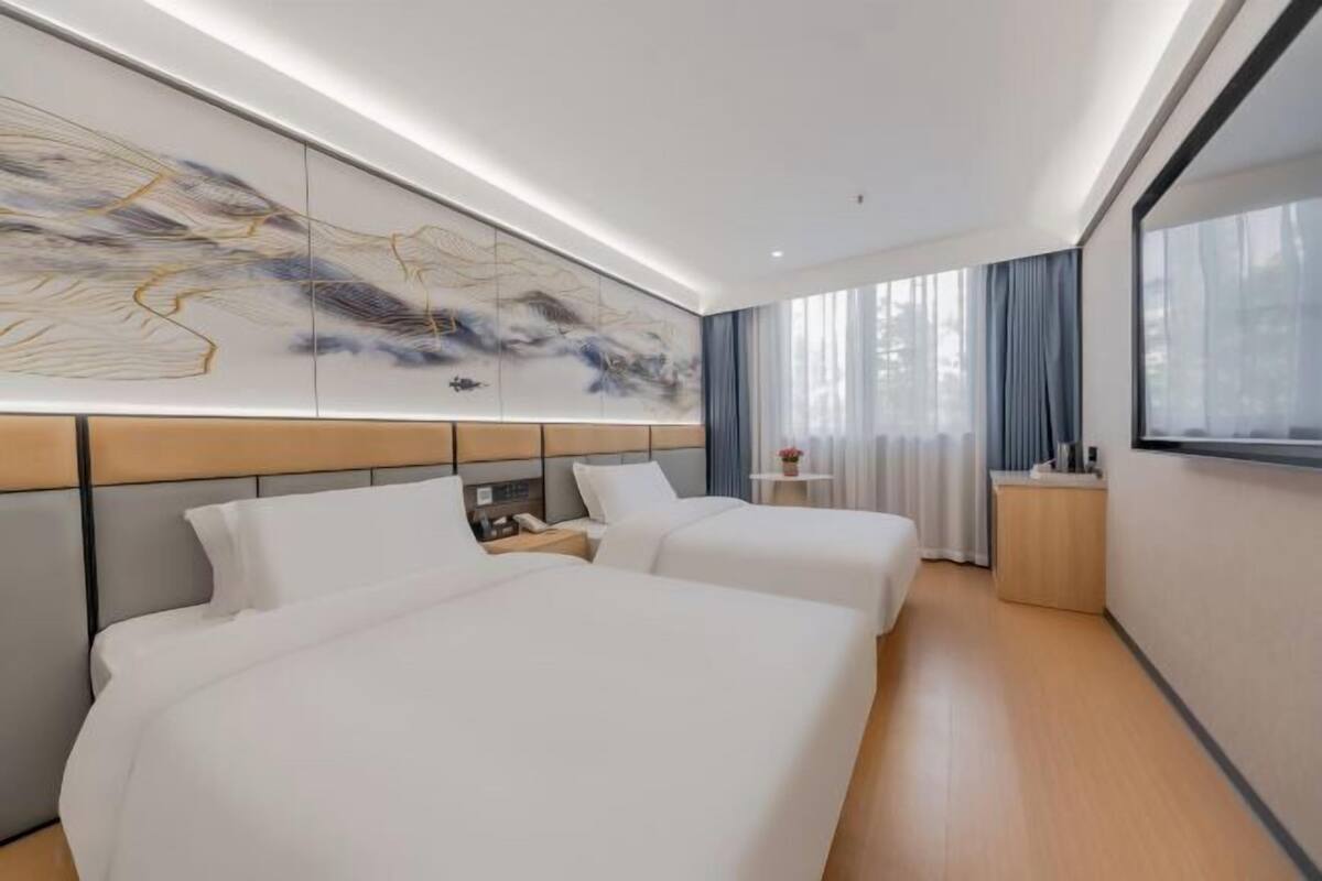 Une chambre d’hôtel moderne avec deux lits, une grande peinture abstraite, une table de chevet et une fenêtre avec des rideaux.