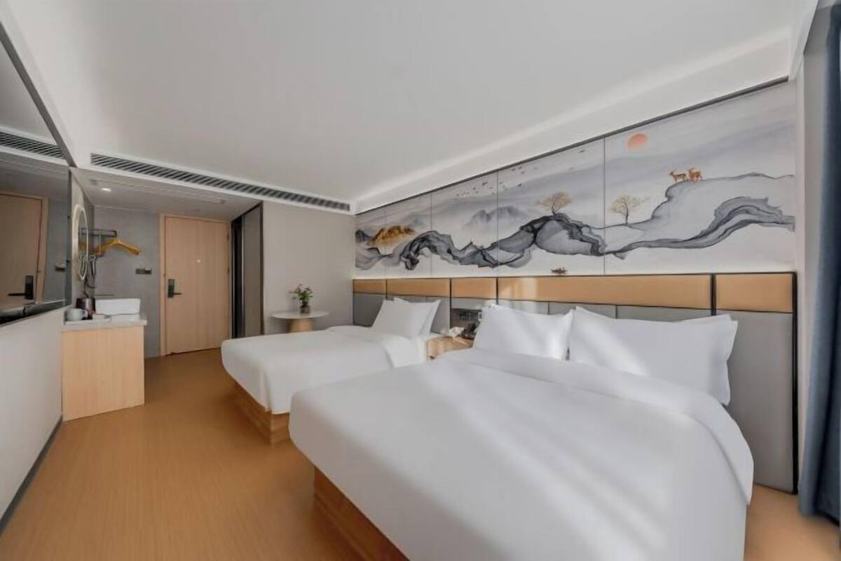 Une chambre d’hôtel avec deux lits, une grande peinture murale, un bureau avec une chaise et un miroir.