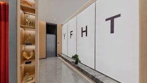 Un pasillo con una estantería de madera que exhibe objetos decorativos, suelo de mármol y una pared con letras grandes que deletrean “YFHT”.