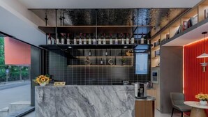 Zona de bar moderna con encimera de mármol, botellas de vino y una cafetera.