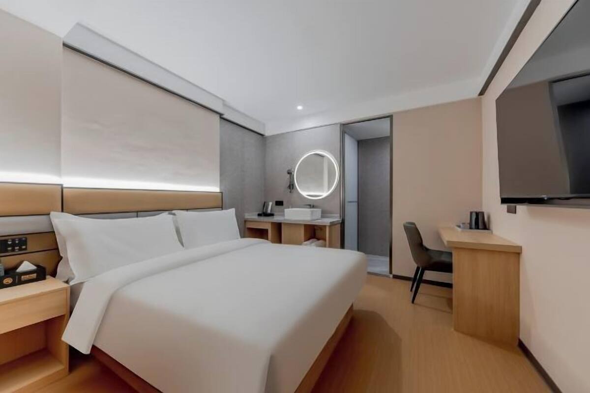 Une chambre d’hôtel moderne équipée d’un lit, d’une table de chevet, d’un bureau, d’une chaise et d’un téléviseur fixé au mur.