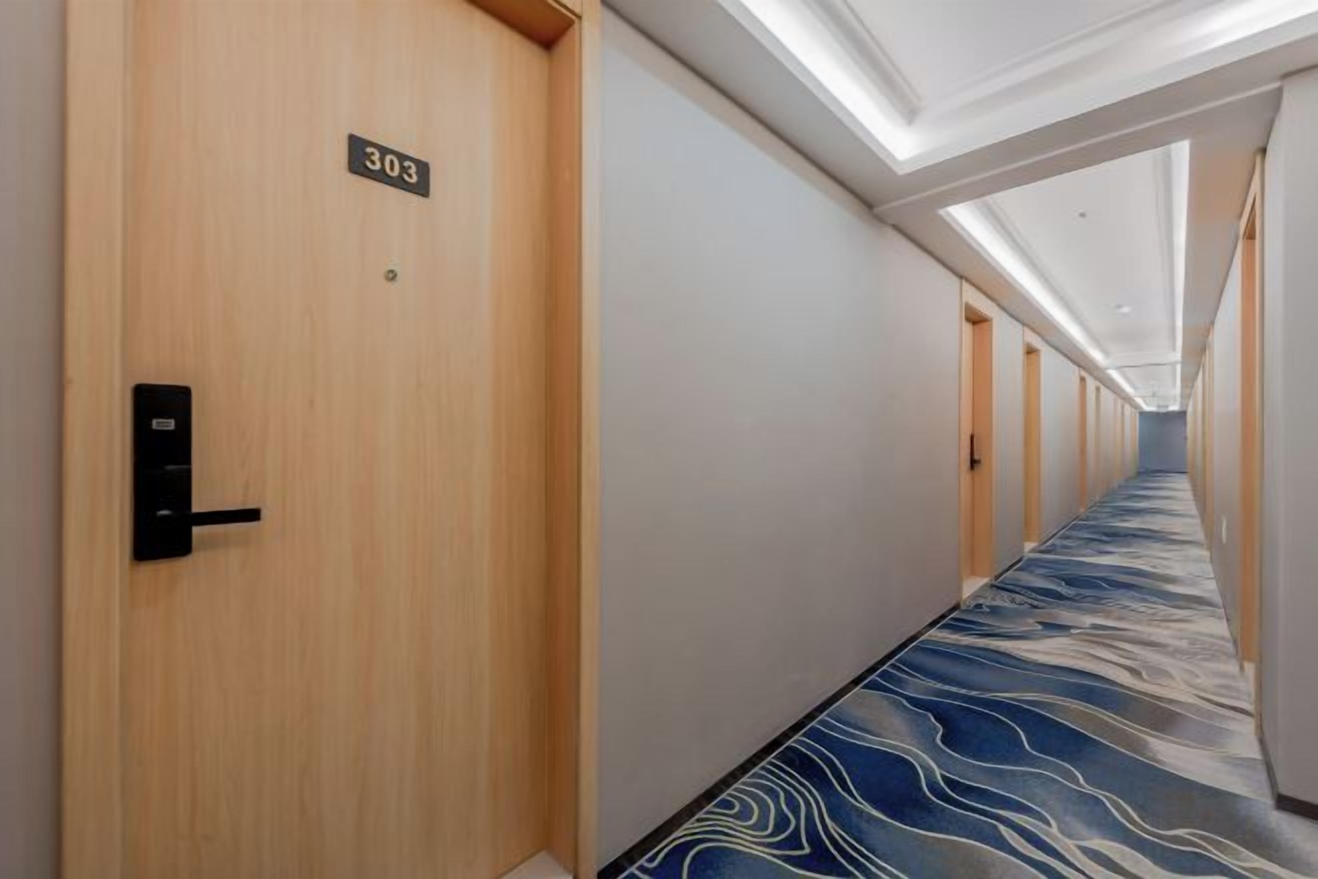 Un pasillo de hotel con alfombra azul estampada, puertas de madera y un letrero con número.