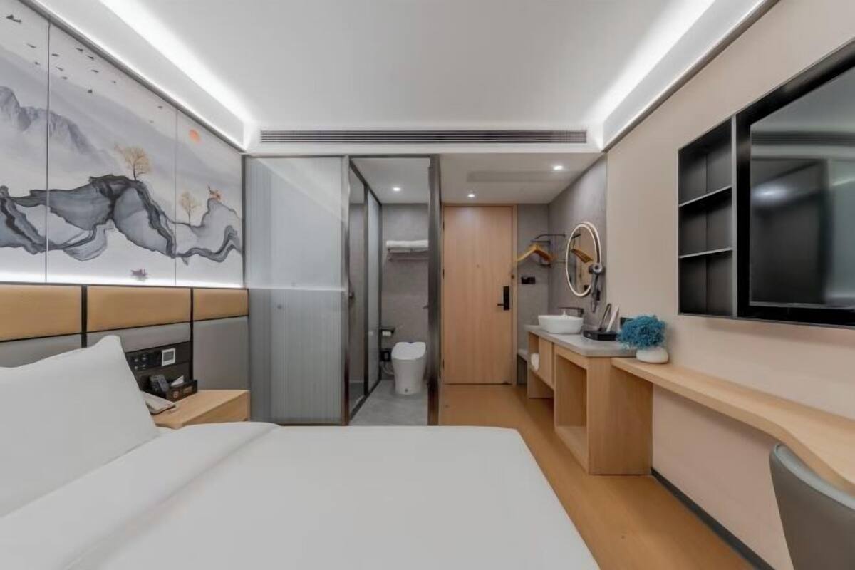 Une chambre d’hôtel moderne équipée d’un lit, d’une salle de bain, d’une télévision et d’une œuvre d’art murale.