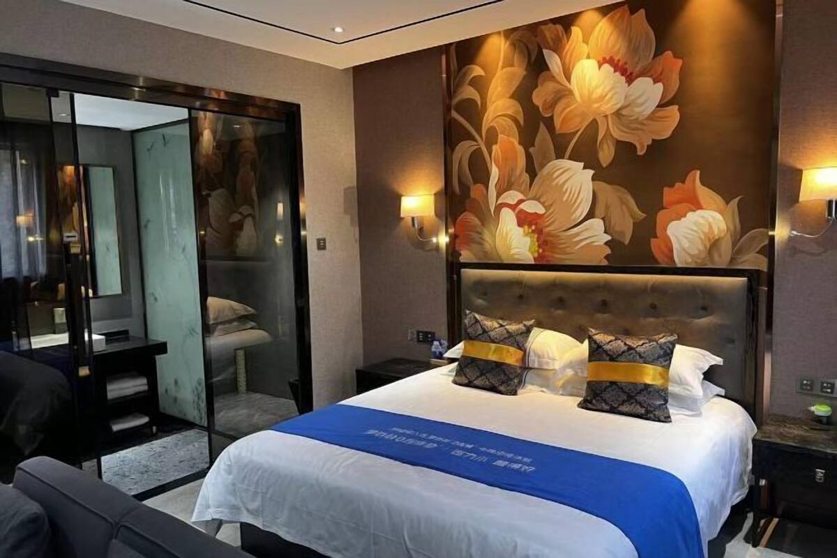 A hotel room with a large bed, a glass partition, and a floral wall mural.