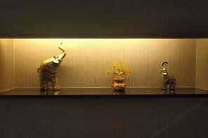 Three decorative items on a shelf: a golden elephant, a vase with yellow flowers, and a golden giraffe. - Meike Hostel (Beijing)