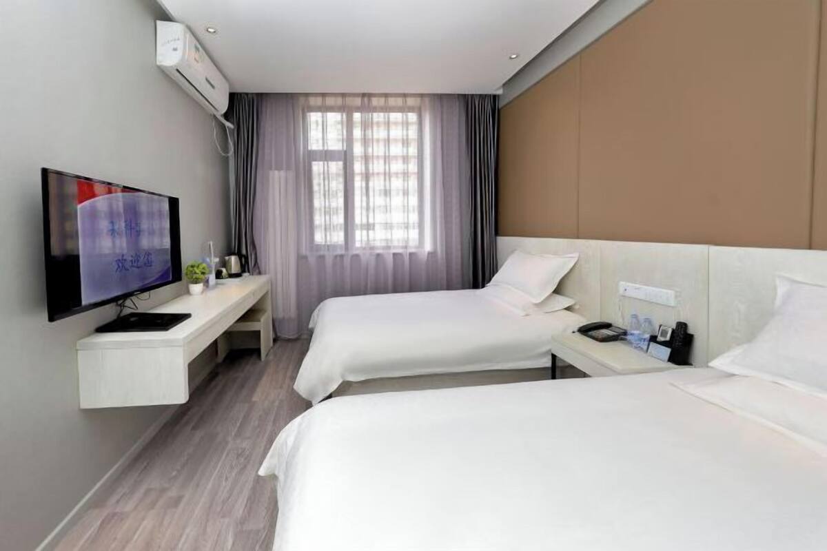 A hotel room with two beds, a TV, a desk, and a window with curtains.