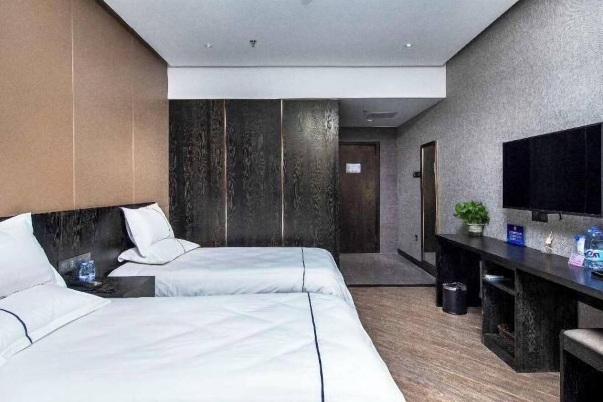 A modern hotel room with two beds, a desk, a flat-screen TV, and a small plant.
