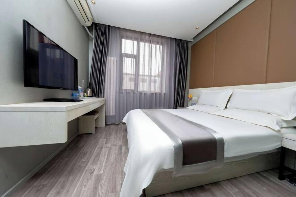 A hotel room with a bed, a TV, a desk, and a window with curtains.