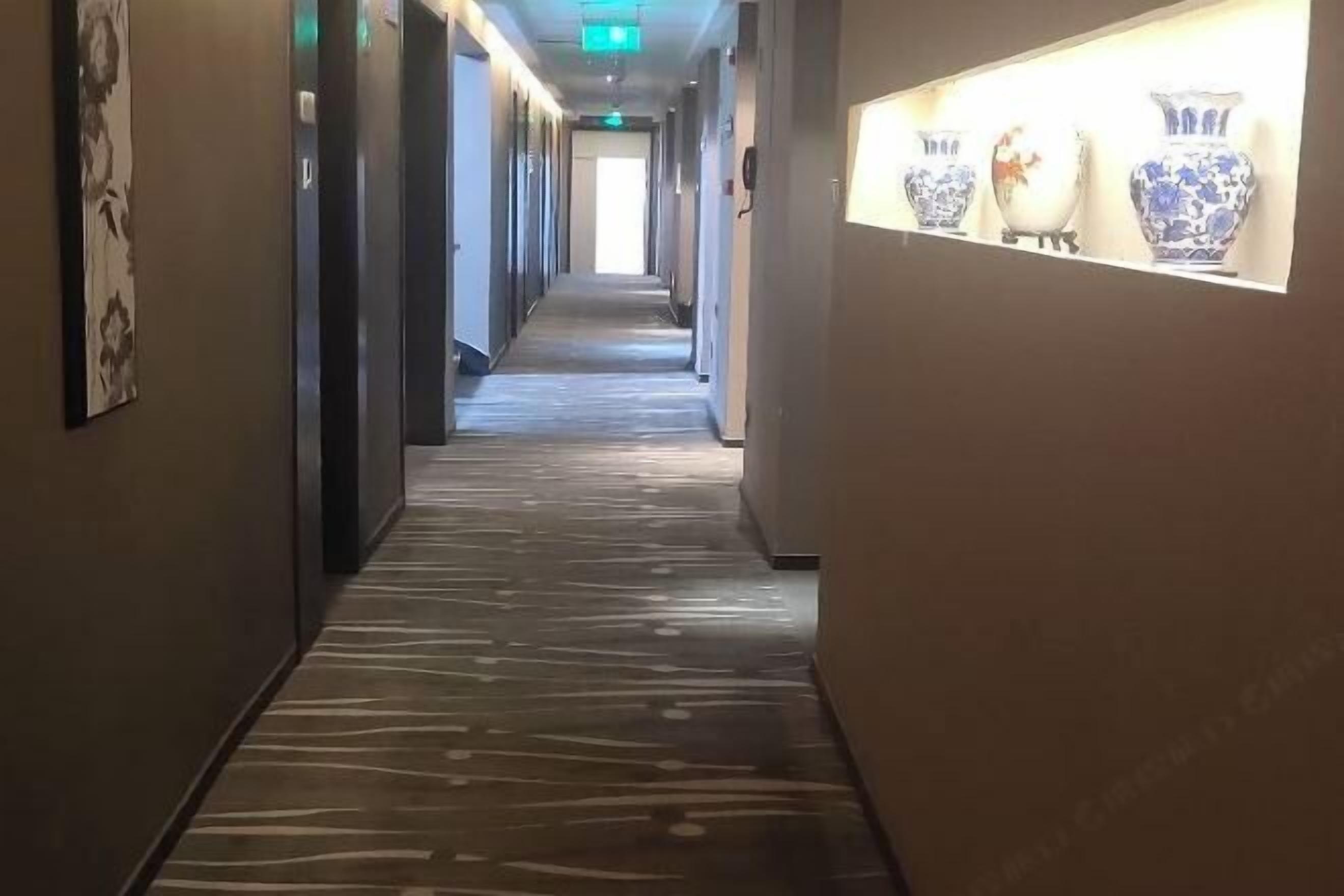 Ein Hotelgang mit Teppichmuster, einer Reihe von Türen und einer Anordnung von Vasen an der rechten Wand.