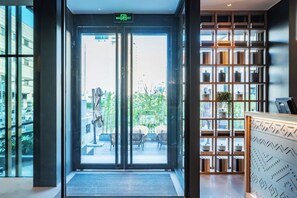 A hotel entrance with a glass door, a reception desk, and a view of the outside.