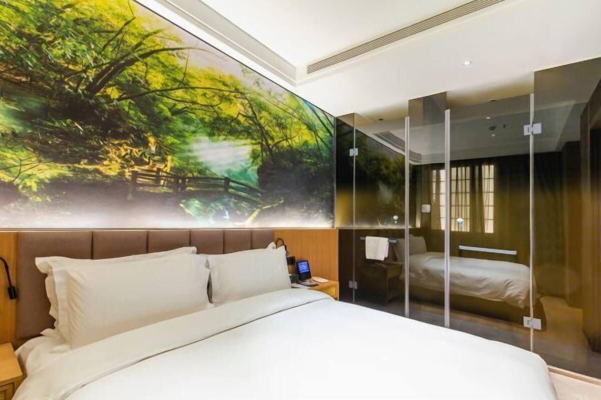Une chambre d’hôtel moderne avec un grand lit, une table de chevet, un ordinateur portable et une grande fenêtre.