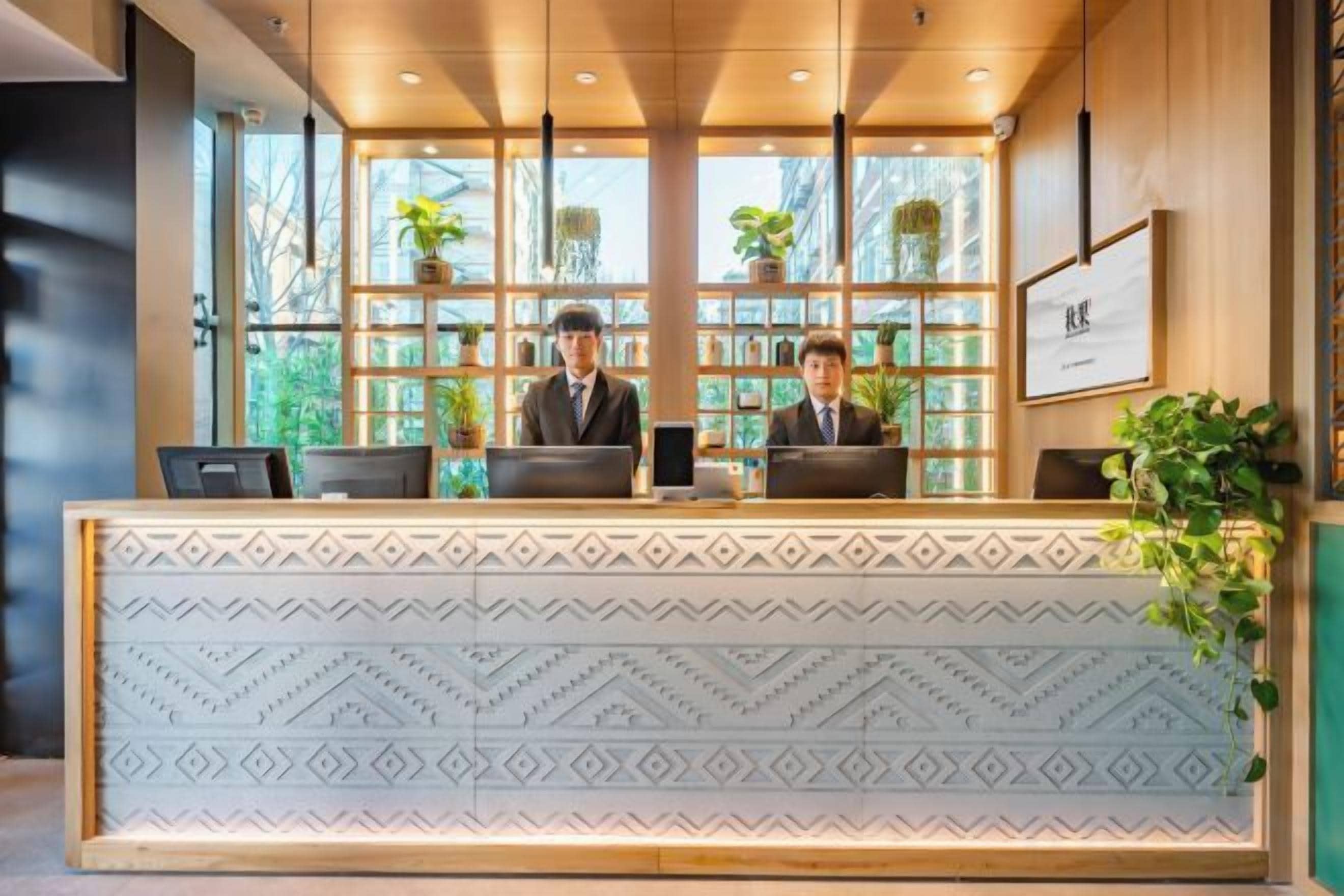 A reception desk with two staff members, a patterned bench, and a bookshelf with plants.