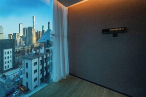 A hotel room with a cityscape view through a window, a directional sign on the wall, and a wooden floor.
