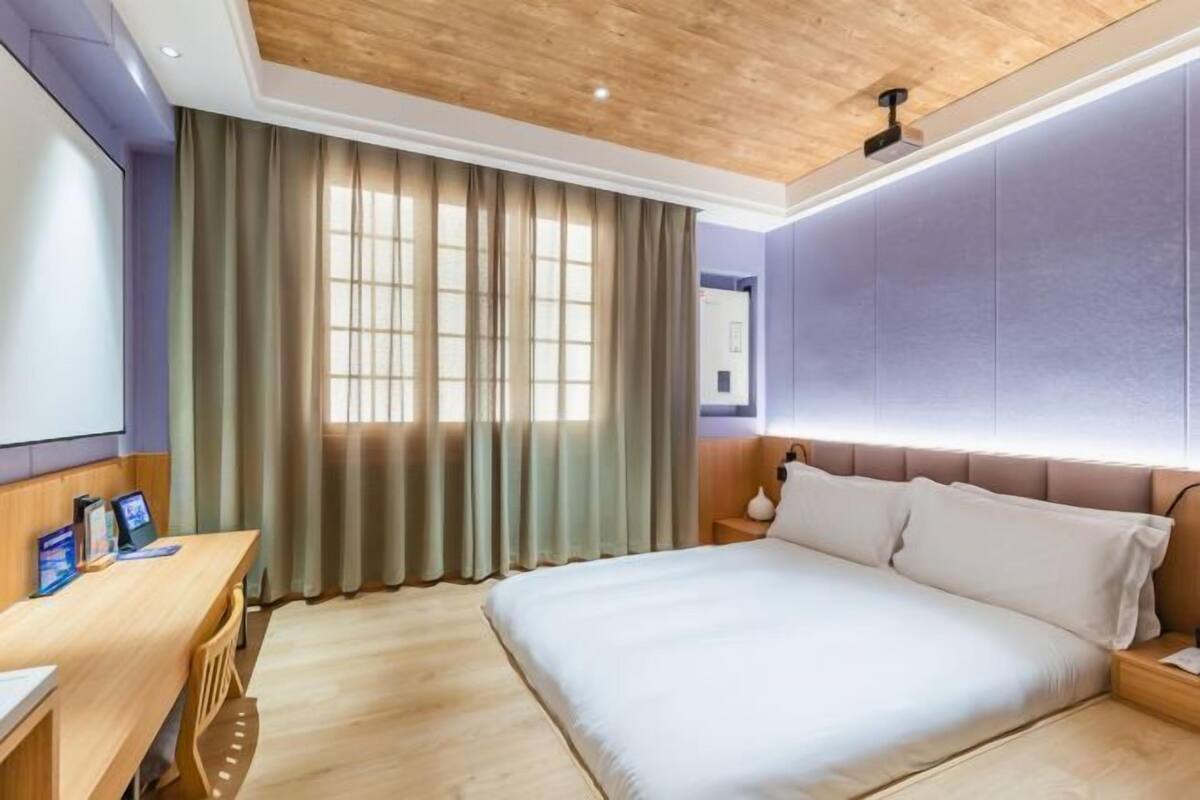 Une chambre d’hôtel avec un plafond en bois, un grand lit, un bureau avec un ordinateur et une fenêtre avec des rideaux.