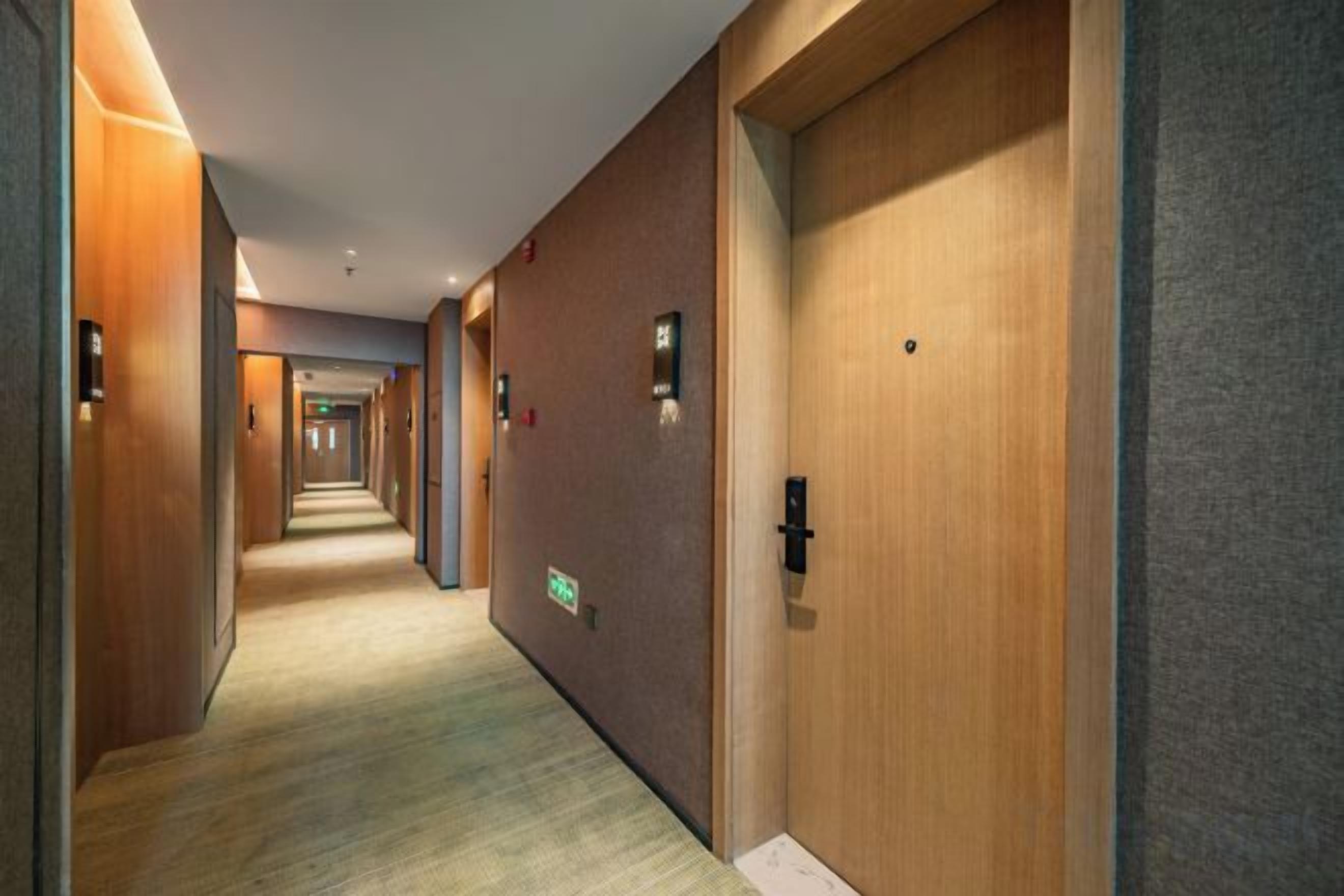 A hotel corridor with wooden doors, carpeted flooring, and wall-mounted light fixtures.
