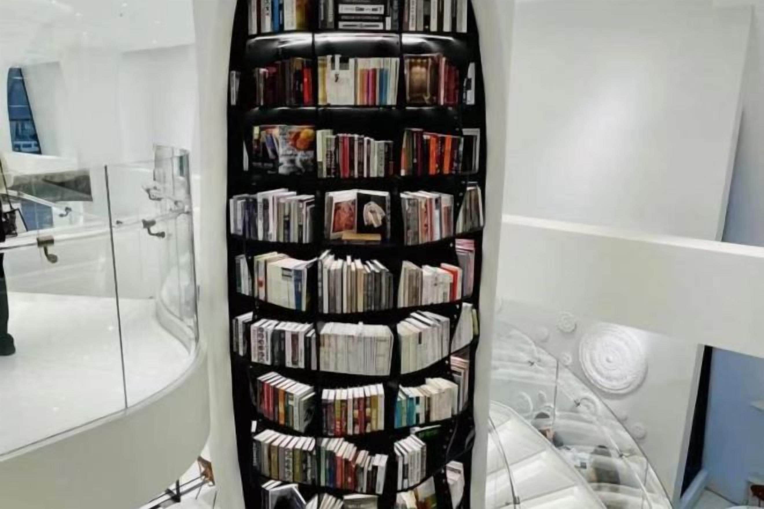 A corner of a room with a black bookshelf filled with books.