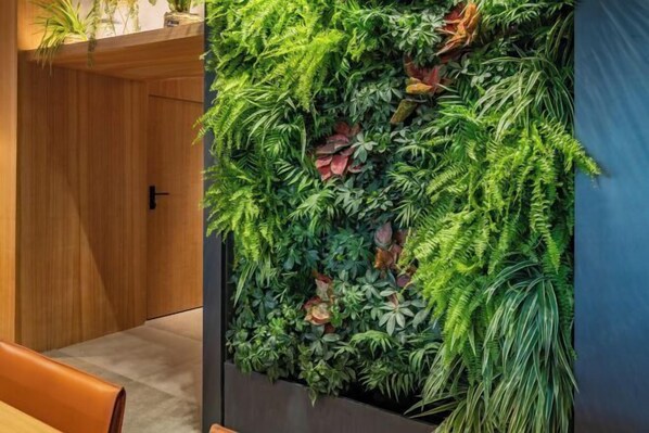 A vertical garden wall with various green plants and some red foliage.