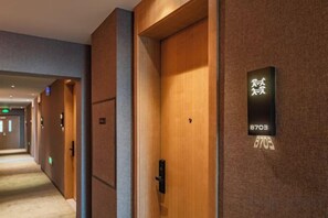 Un pasillo de hotel con puertas, un cartel con números y suelo alfombrado.
