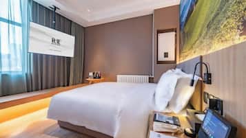 Una habitación de hotel moderna con una cama grande, una mesita de noche con un dispositivo digital y vistas a un cuadro de paisaje en la pared.
