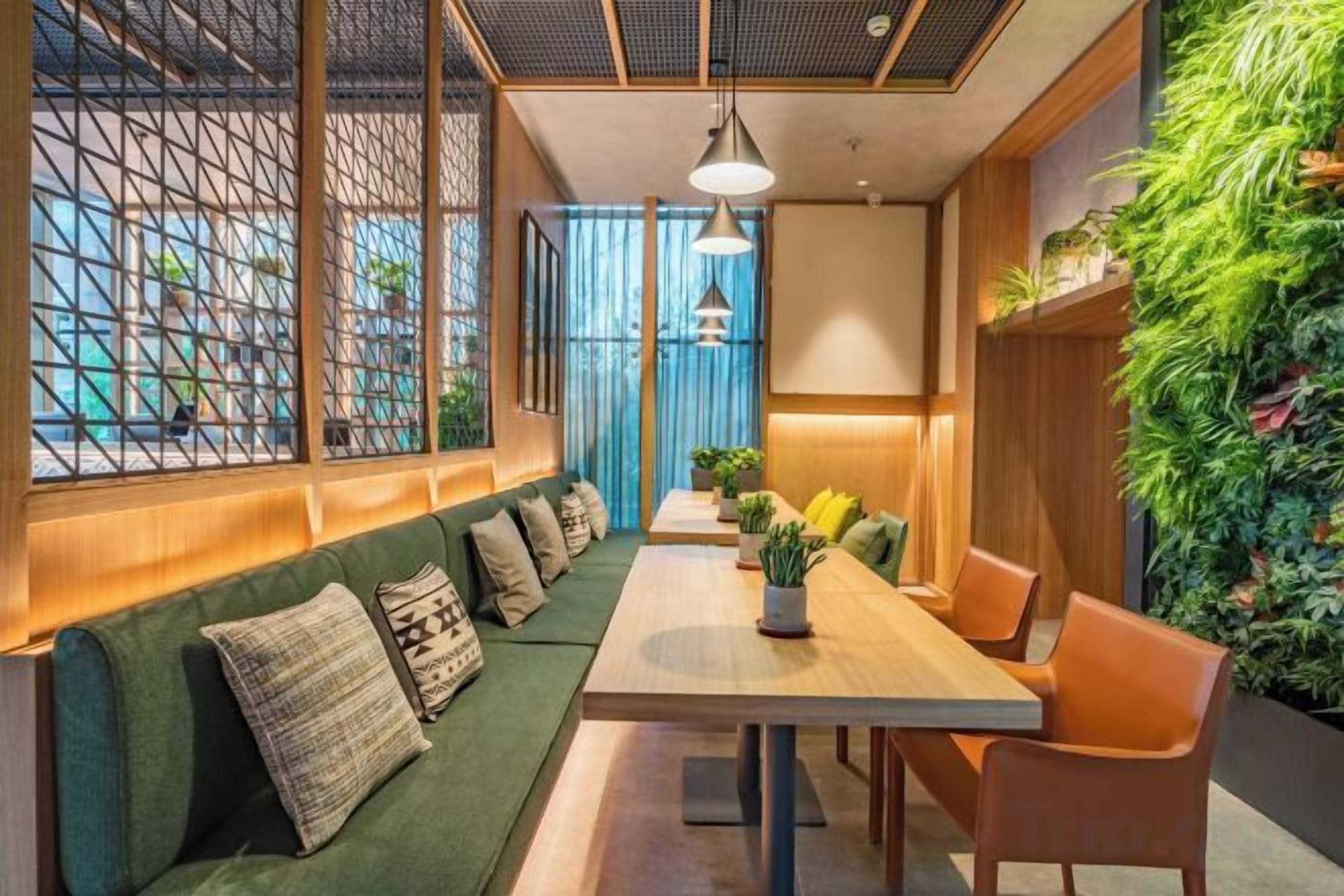 A modern interior with a long table, green cushioned seating, and a vertical garden.