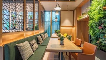 A modern interior with a long table, green cushioned seating, and a vertical garden.