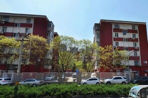 Un edificio residencial de varios pisos con balcones, un estacionamiento con autos y un cielo despejado.