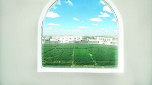 A view through a window of a building with a green field and white structures in the background. - Ivy Canggu (Munggu)