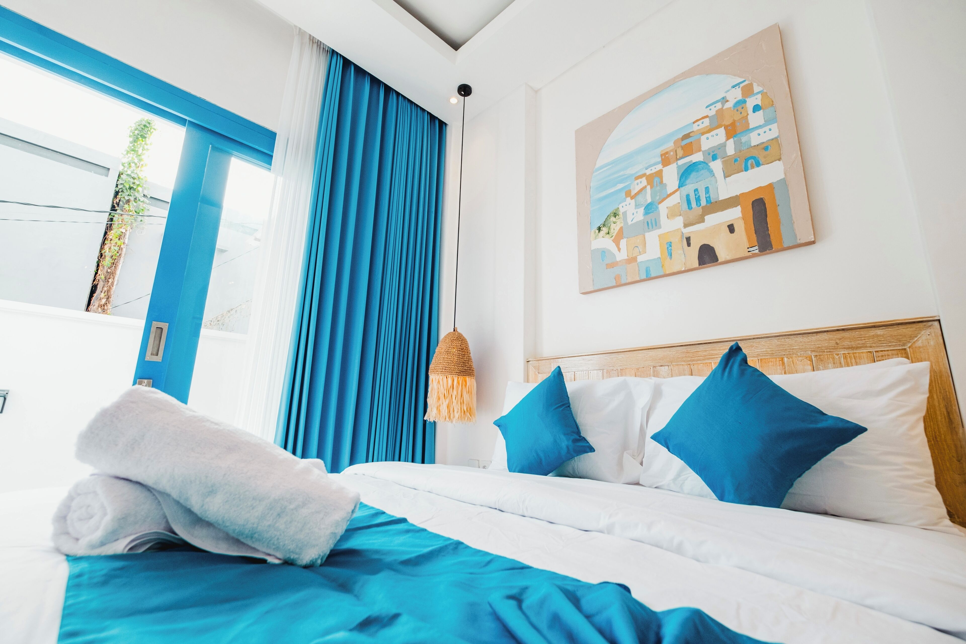 Une chambre d’hôtel avec un lit, des rideaux bleus, un tableau et un luminaire suspendu.