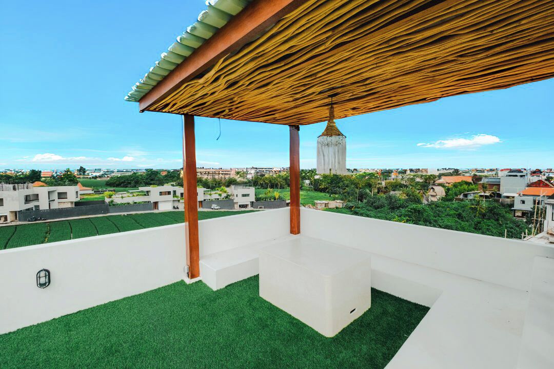 Una terraza en la azotea con pérgola, césped artificial y vistas a la ciudad.