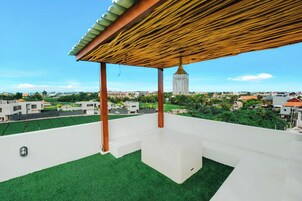 Una terraza en la azotea con pérgola, césped artificial y vistas a la ciudad.