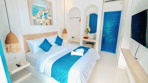 A modern hotel room with a large bed, a flat-screen TV, a painting of a coastal town, and a blue door. - Ivy Canggu (Munggu)