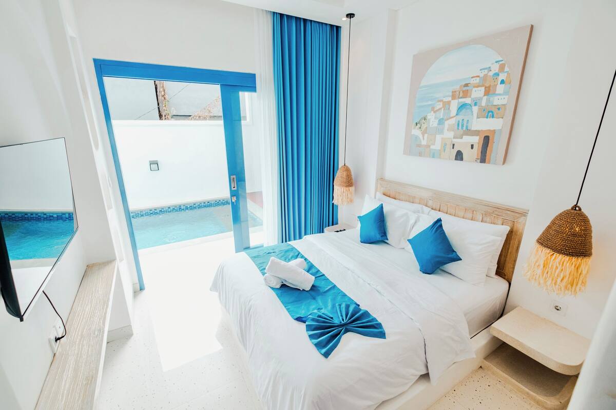 A hotel room with a bed, a TV, a painting, and a view of the pool.