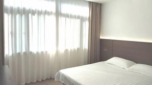 A hotel room with a large window covered by sheer curtains, a bed with white linens, and a neutral-colored headboard. - Zhulian Hostel (Wenzhou)